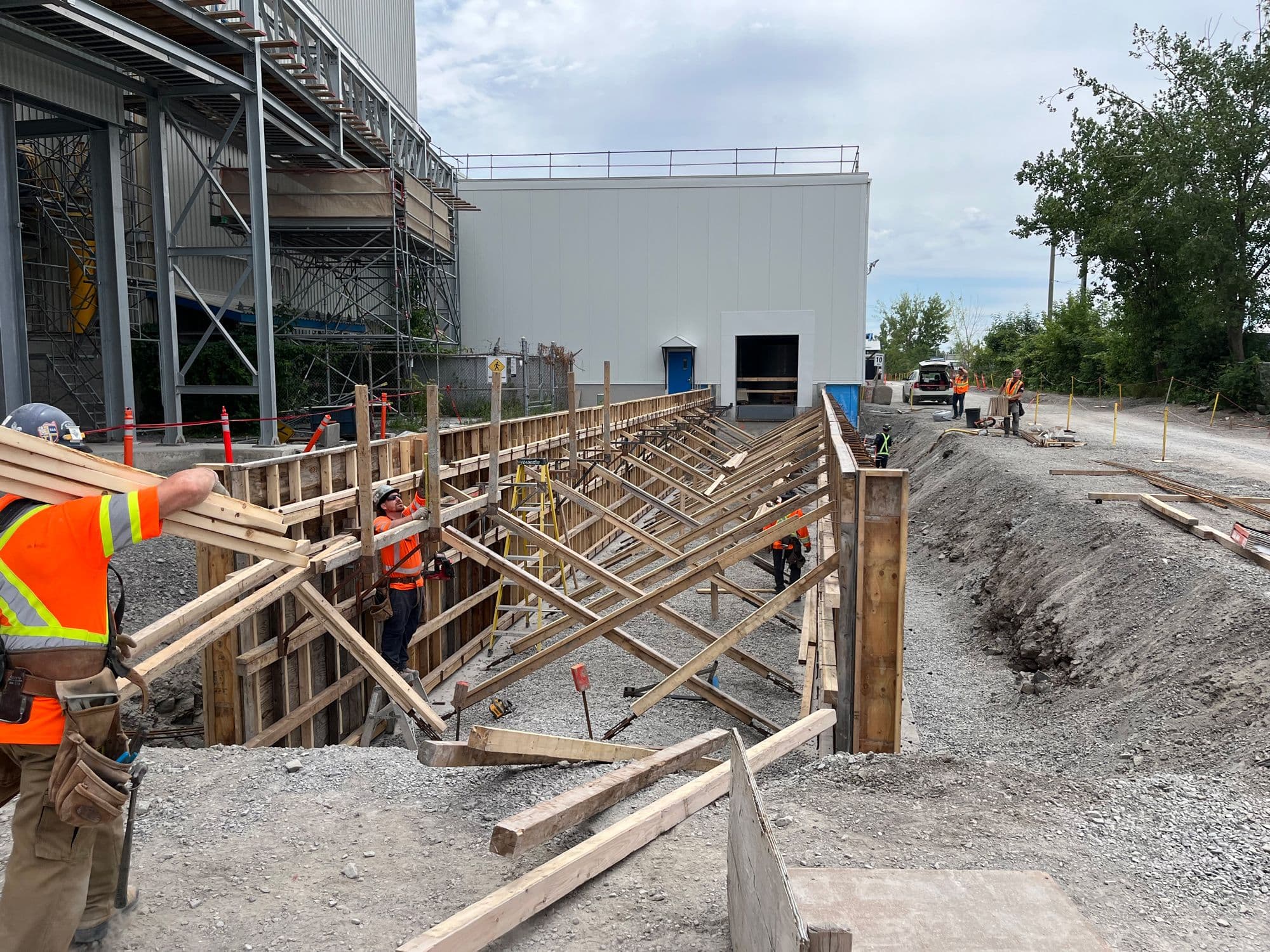 Construction de murs de soutènement en béton avec coffrage de bois sur un site industriel.