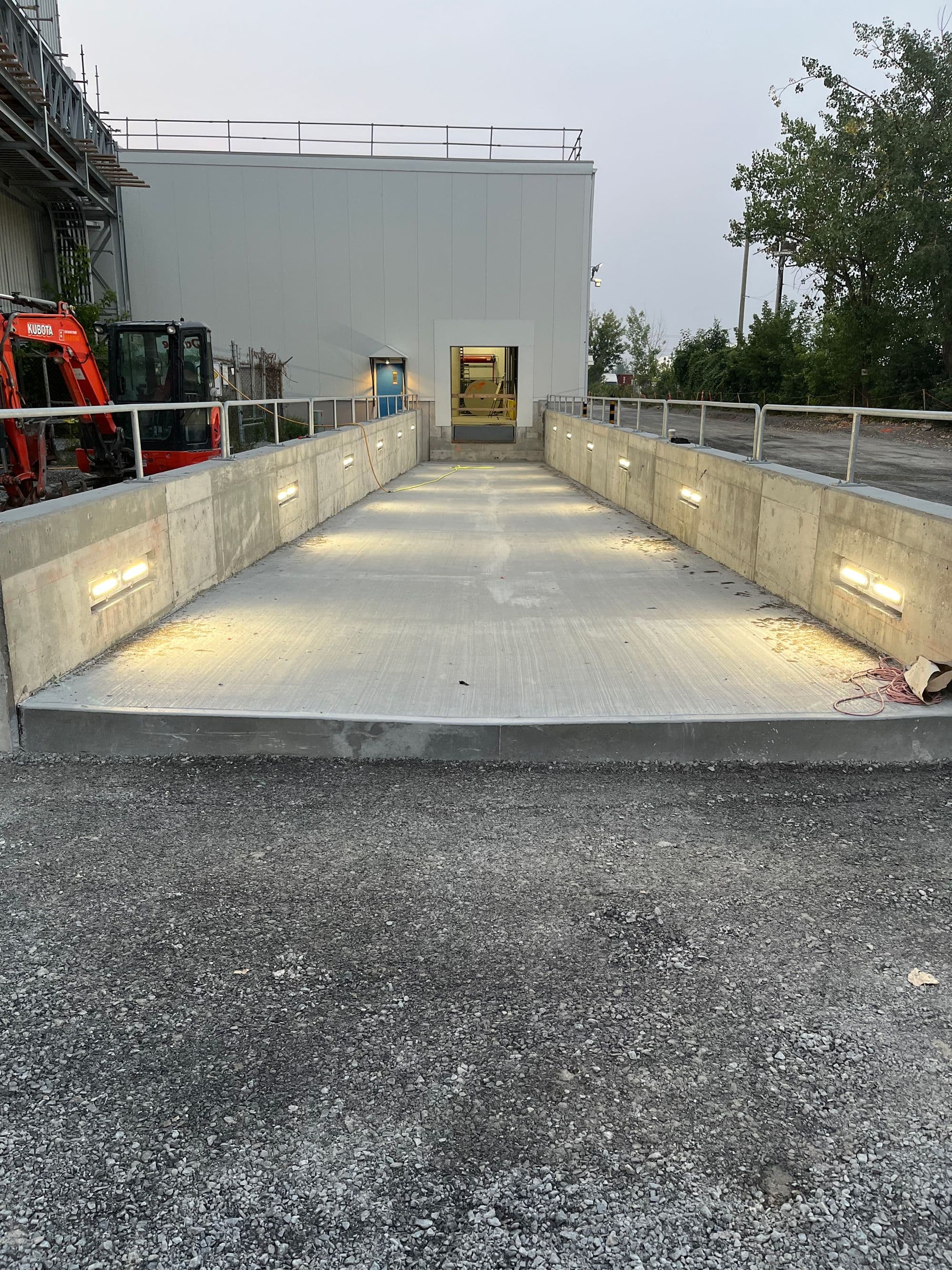 Rampe de béton neuve menant à un bâtiment industriel, réalisée lors de travaux d’infrastructures.